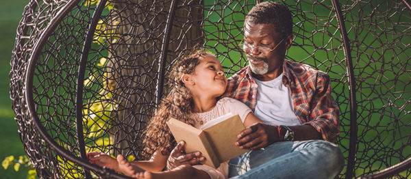 grandchild reading book while sitting in swinging hanging chair with grandfather