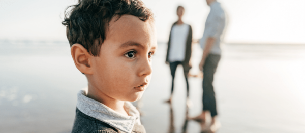 Sad Child Parents on Beach in Background