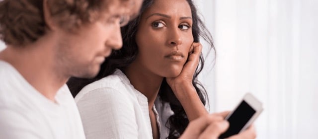 A woman looking at her partner, who is looking at social media accounts on his phone