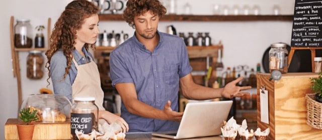 A young man and woman in a restaurant setting looking at a laptop screen discussing family business