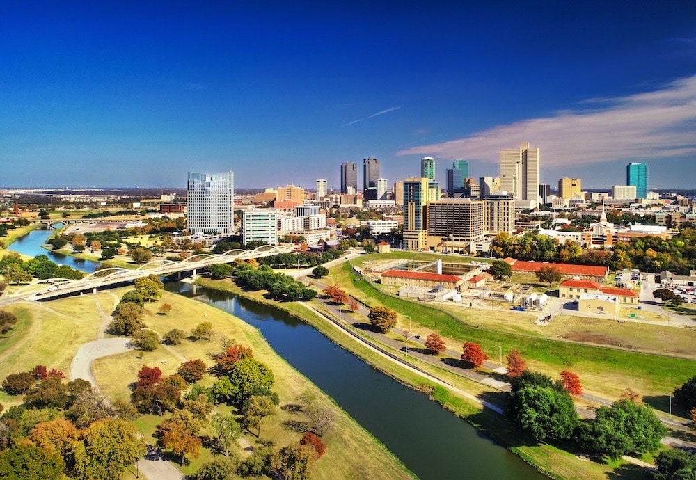 Aerial of Fort Worth during autumn with the Trinity River, bridge, and riverbank parks in the foreground, and Downtown Fort Worth Skyline in the background.